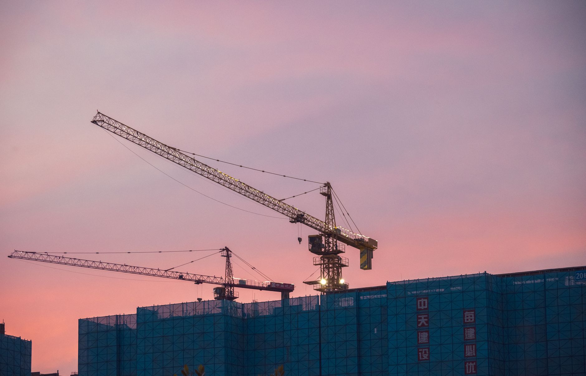 Guindaste de construção civil em meio a prédios em desenvolvimento contra o céu azul.