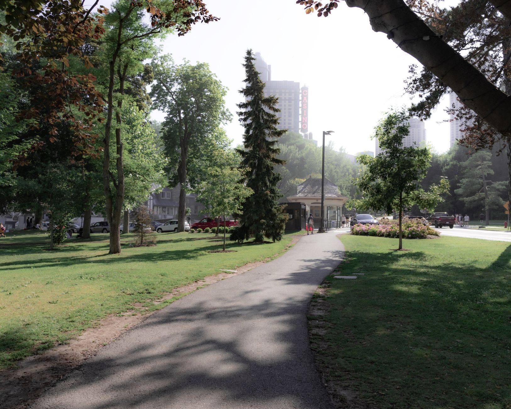 Pista de caminhada asfaltada cercada por gramado e árvores sob um céu azul.
